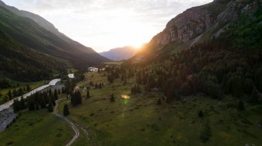 Yeşil vadi ve nehir manzaralı güzel bir gün batımı. Kozalaklı ağaçlar, ormanlar, bir sürü ot. Kaynayan gri bir nehir. Gökyüzündeki bulutlar. Güneş ışınları. Dik uçurumlar