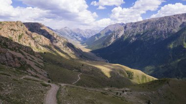 Beyaz bir SUV nehir boyunca uzanan bir vadi boyunca bir dağ yolunun üstesinden gelir. Uçurumlu yeşil alanlar. Dik uçurumlar ve yoldaki büyük kayalar. Keskin bir iniş ve tepe manzarası. Noel ağaçları