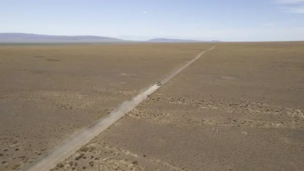 Bozkırda tozlu bir yolda beyaz bir SUV hızlı gidiyor. Tekerleklerin altından ve arabanın çatısından toz bulutları uçar. Cip toprak bir yolu kolayca geçer. Mavi gökyüzü ve beyaz bulutlar.