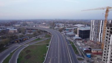 Yol kenarında yüksek evler inşa ediliyor. Almaty şehri. Yeni çok katlı binalar inşa ediliyor. İnşaatçılar, vinç, makineler çalışıyor. İHA 'dan evlerin ve yolların havadan görüntüsü.