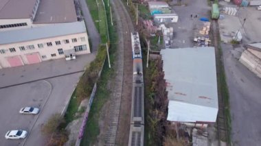 Modern bir tren Almaty şehrinden geçer. Demiryolu depolardan ve özel binalardan geçiyor. Yakınlarda alçak bir köprü var. Kargo yüklemek için turna. Şehir emisyondan dolayı dumanlı.