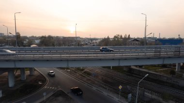 Şehirden geçen köprünün drone görüntüsü. Arabalardan kamyonlara farklı arabalar geçiyor. Serbest şerit. Gün batımında sisli bir şehrin arka planına karşı. Fabrikanın bacaları tütüyor.