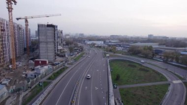 Yol kenarında yüksek evler inşa ediliyor. Almaty şehri. Yeni çok katlı binalar inşa ediliyor. İnşaatçılar, vinç, makineler çalışıyor. İHA 'dan evlerin ve yolların havadan görüntüsü.