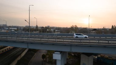 Şehirden geçen köprünün drone görüntüsü. Arabalardan kamyonlara farklı arabalar geçiyor. Serbest şerit. Gün batımında sisli bir şehrin arka planına karşı. Fabrikanın bacaları tütüyor.