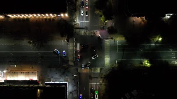 夜間交差点の無人機からの空中ビュー 道路に沿って車やバスからの小さな交通が動いている 提灯は明るく輝いている 信号が点滅している警察の車で通路がブロックされています — ストック動画