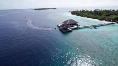 Yeşil bir ada boyunca bir jet ski okyanusta yüzer. Arkalarında beyaz dalgalar bırakarak. Koyu mavi okyanus suyu. Maldivler. Yeşil bir ada ve turkuaz bir resif. İHA 'nın üst görüntüsü. Hızlı hız