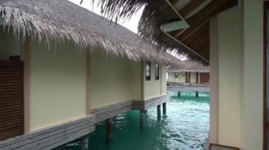 Bungalovun sazdan damlayan damlaları. Deniz kıyısındaki villalar. Yeşil renkli ışık dalgaları ve turkuaz su rengi. Yağmurdan hafif köpük, bulutlu gri gökyüzü