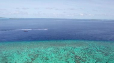 Yeşil bir ada boyunca bir jet ski okyanusta yüzer. Arkalarında beyaz dalgalar bırakarak. Koyu mavi okyanus suyu. Maldivler. Yeşil bir ada ve turkuaz bir resif. İHA 'nın üst görüntüsü. Hızlı hız