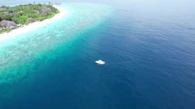 Beyaz bir tekne okyanusta kıyıya doğru gidiyor. İHA 'dan turkuazdan koyu maviye suyun gradyan görüntüsü. Adanın güzel resifleri. Bulutlu gökyüzü. Mavi Göl
