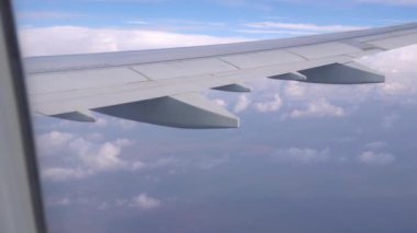 Beyaz bulutların uçak penceresinden görünen manzara. Bir uçağın gümüş kanadı. Kahverengi toprak bazı yerlerde görülebilir. Bulutların gölgeleri komşu bulutların üzerine düşüyor. Uçağın penceresi..