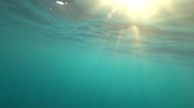Turkuaz berrak okyanus suyu ve güneş ışınları. Hızlı hareket hızından kabarcıklar. Işıklı dalgalar ve derin depresyonlar. Suyun altında hızla çekim yapmak. Yunus arayışında