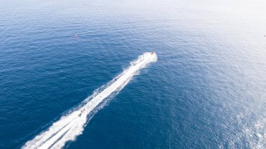 A water scooter cuts through the ocean creating waves. The dark blue water gradually turns into light from the rays of the sun. Long waves and scooter tracks. Top view from a drone. Fun at sea clipart