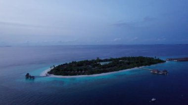 Okyanustaki bir adadan gün batımının en üst görüntüsü. Pembe renkli büyük siyah bulutlar. Turkuaz okyanus suyu, kumsalın beyaz kumu. Yeşil palmiye ağaçları ve ağaçlar. Maldivler. Su ayna gibidir.