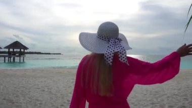 Pembe beyaz şapkalı bir kız sahile gider. Beyaz mercan kumu, turkuaz su parıldıyor ve karanlık bir taneye dönüşüyor. Gri gökyüzü ve gün batımı. Sudaki balkonlar görülebilir. Adada hayat.