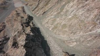 Vadideki dik uçurumlar boyunca bir FPV insansız hava aracına atlamak. Güneş ışınları tepenin arkasından geliyor. Büyük kayalar, yeşil çimenler ve vadiden aşağı akan bir nehir. Dağların arasında uçarak