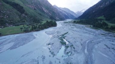 Araba nehir boyunca yeşil bir geçitten geçiyor. Uzun otlar ve kozalaklı ağaçlar büyür. Bazı yerlerde yollarda su birikintileri var. Nehir kenarındaki taşlar görülebilir. SUV sessizce gidiyor.