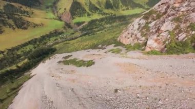Uçurumdan nehre giden bir FPV insansız hava aracına atlamak. Dağlık bölge. Aşağı uçarken, kozalaklı ağaçlar, kayalar ve yeşil otlar ortaya çıkar. Aşağıda berrak ve sakin bir nehir görülebilir. Küçük bir vadi..