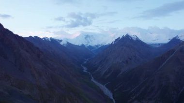Uzakta kar zirveleri olan vadi manzarası. İnsansız hava aracı sorunsuz uçuyor. Vadinin içinden bir nehir akıyor. Khan Tengri 'nin görkemli zirvesine sahip yüksek dağlar. Buzdan yapılmış mermer bir duvar. Bulutlu