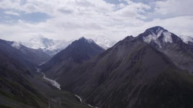 Uzakta kar zirveleri olan vadi manzarası. İnsansız hava aracı sorunsuz uçuyor. Vadinin içinden bir nehir akıyor. Khan Tengri 'nin görkemli zirvesine sahip yüksek dağlar. Buzdan yapılmış mermer bir duvar. Bulutlu
