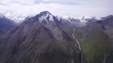 Uzakta kar zirveleri olan vadi manzarası. İnsansız hava aracı sorunsuz uçuyor. Vadinin içinden bir nehir akıyor. Khan Tengri 'nin görkemli zirvesine sahip yüksek dağlar. Buzdan yapılmış mermer bir duvar. Bulutlu