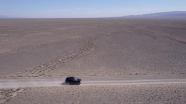 Bozkırda tozlu bir yolda siyah bir SUV hızlı gidiyor. Tekerleklerin altından ve arabanın çatısından toz bulutları uçuyor. Araba toprak bir yolun üstesinden kolayca gelir. Mavi gökyüzü ve beyaz bulutlar.