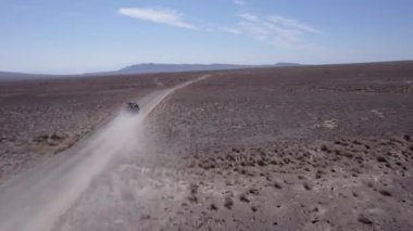 Bozkırda tozlu bir yolda siyah bir SUV hızlı gidiyor. Tekerleklerin altından ve arabanın çatısından toz bulutları uçuyor. Araba toprak bir yolun üstesinden kolayca gelir. Mavi gökyüzü ve beyaz bulutlar.