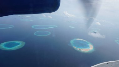 Maldivler adalarının çarpıcı hava manzarası benzersiz mercan oluşumlarını ve deniz uçağının penceresinden görülen kristal berraklığında turkuaz sularını gösteriyor.