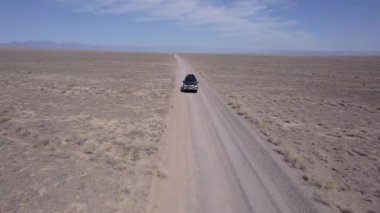 Bozkırda tozlu bir yolda siyah bir SUV hızlı gidiyor. Tekerleklerin altından ve arabanın çatısından toz bulutları uçuyor. Araba toprak bir yolun üstesinden kolayca gelir. Mavi gökyüzü ve beyaz bulutlar.