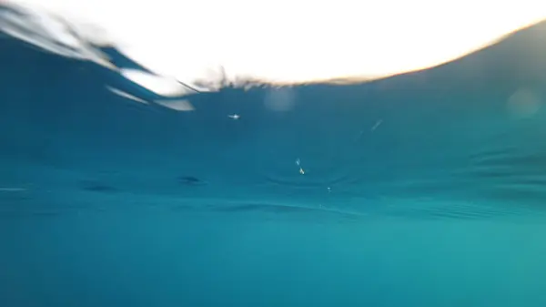 Sualtı görüntüsü, parıldayan ışık yansımaları ve hafif dalgalarla yüzeyi yakalıyor. Huzurlu ve huzurlu bir atmosfer yaratıyor.