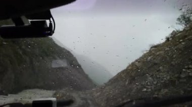Fırtınaya karşı arabanın ön camından bak. Şiddetli yağmur yağıyor ve şimşek çakıyor. Kayalarla dolu bir vadiden geçen tehlikeli kayalık bir yol. Gri, akan bir nehir akıyor. Yoğun sis
