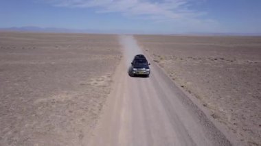 Bozkırda tozlu bir yolda siyah bir SUV hızlı gidiyor. Tekerleklerin altından ve arabanın çatısından toz bulutları uçuyor. Araba toprak bir yolun üstesinden kolayca gelir. Mavi gökyüzü ve beyaz bulutlar.