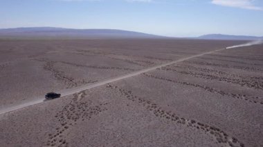 Bozkırda tozlu bir yolda siyah bir SUV hızlı gidiyor. Tekerleklerin altından ve arabanın çatısından toz bulutları uçuyor. Araba toprak bir yolun üstesinden kolayca gelir. Mavi gökyüzü ve beyaz bulutlar.