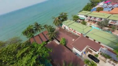 Çarpıcı hava manzaraları, yemyeşil tepeler ve tropik okyanusun kristal berrak turkuaz suları arasında yuva yapmış canlı bir tatil köyünü gösteriyor. Resimli bir tatil cenneti manzarası sunuyor.