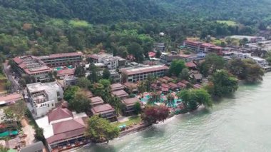 Geleneksel Thai mimari otelleri ve turkuaz berrak suları ile Koh Chang adasındaki bir tatil köyünü çevreleyen yemyeşil bir orman,
