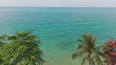Turkuaz okyanus dalgaları Koh Chang Adası, Tayland 'ın kumlu sahillerinde yavaşça dolaşır, yemyeşil bitki örtüsü ve rüzgarda sallanan palmiye ağaçları, sakin bir tropikal cennet yaratır.