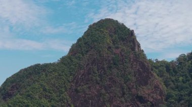 Yeşil bitki örtüsü ve engebeli kayalık yamaçlarla yükselen Koh Chang 'in dağ zirvesi parlak mavi gökyüzünün altında ince bulutlarla dağılmış el değmemiş tropikal manzarayı ortaya çıkarıyor.