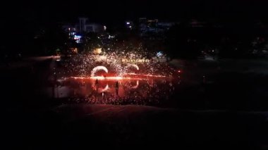 Yetenekli ateş dansçıları hipnotik ışık desenleri yaratırken alevli aksesuarları çeviriyorlar, karanlık tropik plajları büyüleyici performans hareketleri ile aydınlatıyorlar.