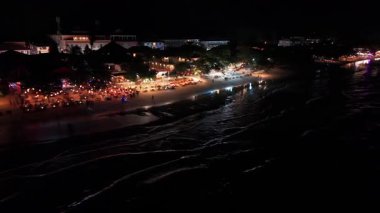Sahil şeridinde yumuşak dalgaların dolaştığı gece sahneleri, turistler renkli aydınlatma altında canlı sahil restoranları ve barların keyfini çıkararak, neşeli tropikal atmosfer yaratıyorlar.