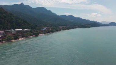 Turkuaz su, açık mavi gökyüzünün altında otellerin ve tatil beldelerinin yemyeşil bitki örtüsünün ortasında durduğu Koh Chang adasının kumlu sahilinde nazikçe süzülür.