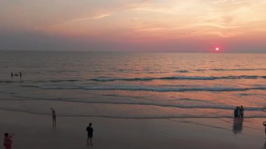 Turistler ve aileler, Koh Chang Adası, Tayland sahillerinde güzel bir günbatımının tadını çıkarıyor. Fotoğraf çekiyor ve sığ sularda oynuyorlar.