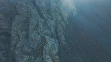 Vadideki dik uçurumlar boyunca bir FPV insansız hava aracına atlamak. Güneş ışınları tepenin arkasından geliyor. Büyük kayalar, yeşil çimenler ve vadiden aşağı akan bir nehir. Dağların arasında uçarak
