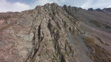 Vadideki dik uçurumlar boyunca bir FPV insansız hava aracına atlamak. Güneş ışınları tepenin arkasından geliyor. Büyük kayalar, yeşil çimenler ve vadiden aşağı akan bir nehir. Dağların arasında uçarak
