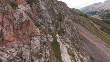 Uçurumdan nehre giden bir FPV insansız hava aracına atlamak. Dağlık bölge. Aşağı uçarken, kozalaklı ağaçlar, kayalar ve yeşil otlar ortaya çıkar. Aşağıda berrak ve sakin bir nehir görülebilir. Küçük bir vadi..