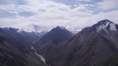 Uzakta kar zirveleri olan vadi manzarası. İnsansız hava aracı sorunsuz uçuyor. Vadinin içinden bir nehir akıyor. Khan Tengri 'nin görkemli zirvesine sahip yüksek dağlar. Buzdan yapılmış mermer bir duvar. Bulutlu