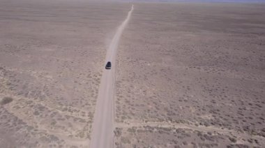 Bozkırda tozlu bir yolda siyah bir SUV hızlı gidiyor. Tekerleklerin altından ve arabanın çatısından toz bulutları uçuyor. Araba toprak bir yolun üstesinden kolayca gelir. Mavi gökyüzü ve beyaz bulutlar.