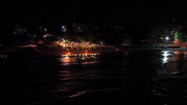 Gece vakti plaj kutlamalarında tropikal tatil beldesinin arka planında sahne alan ateş dansçıları dramatik gölgeler oluşturup coşkulu enerjiyle heyecanlı kalabalığı aydınlatıyorlar.