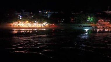 Sıcak ışıklar parıldıyor sahilde toplanıyor, geceyi aydınlatıyor enerjik kalabalık karanlık gökyüzünün altında tropikal bir akşamın tadını çıkarıyor.