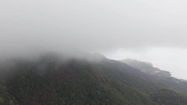 Puslu beyaz sis, Koh Chang 'deki yeşil dağ yamaçlarını yavaş yavaş kaplıyor. Kısmen karanlık tropikal kıyı şeridi dramatik hava dönüşümüyle yuvarlanan bulutların altındaki huzurlu manzarayı ortaya çıkarıyor