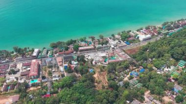 Turkuaz sular koh chang adasının genişleyen sahil şeridine nazikçe uzanır, yemyeşil ve gelişmiş alanların karışımını sergiler, dinamik ve gelişmekte olan tropikal bir manzara yaratır.