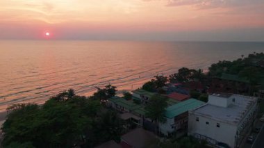 Gökyüzünde pembe ve turuncu renkler boyayarak canlı gün batımı, Tayland 'daki Koh Chang Adası' ndaki tropik sahil beldesinin yakınındaki kumlu kıyı şeridini nazikçe okşayan dalgaları nazikçe yıkamak.